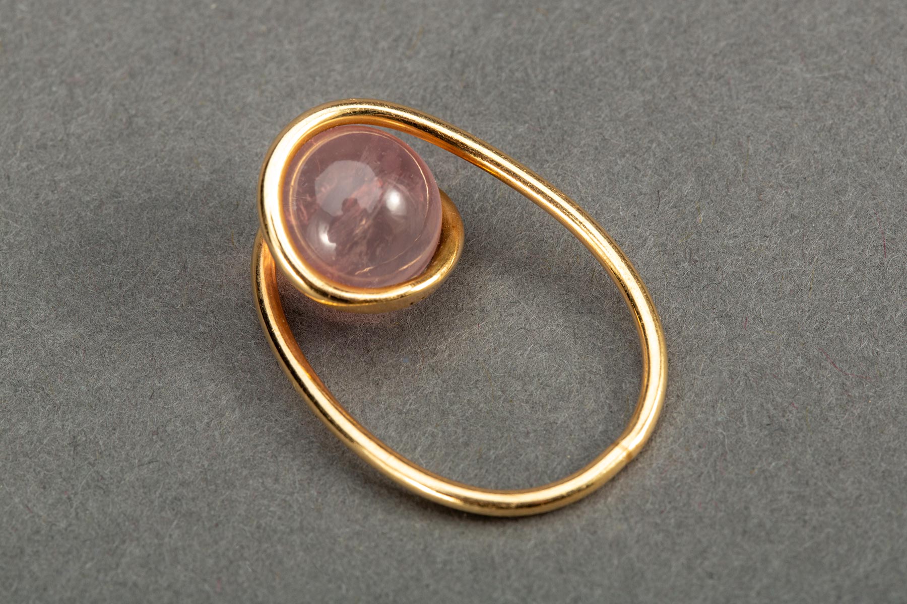 Thin and shiny gold wire organically formed around a round, pink-colored piece of rose quartz