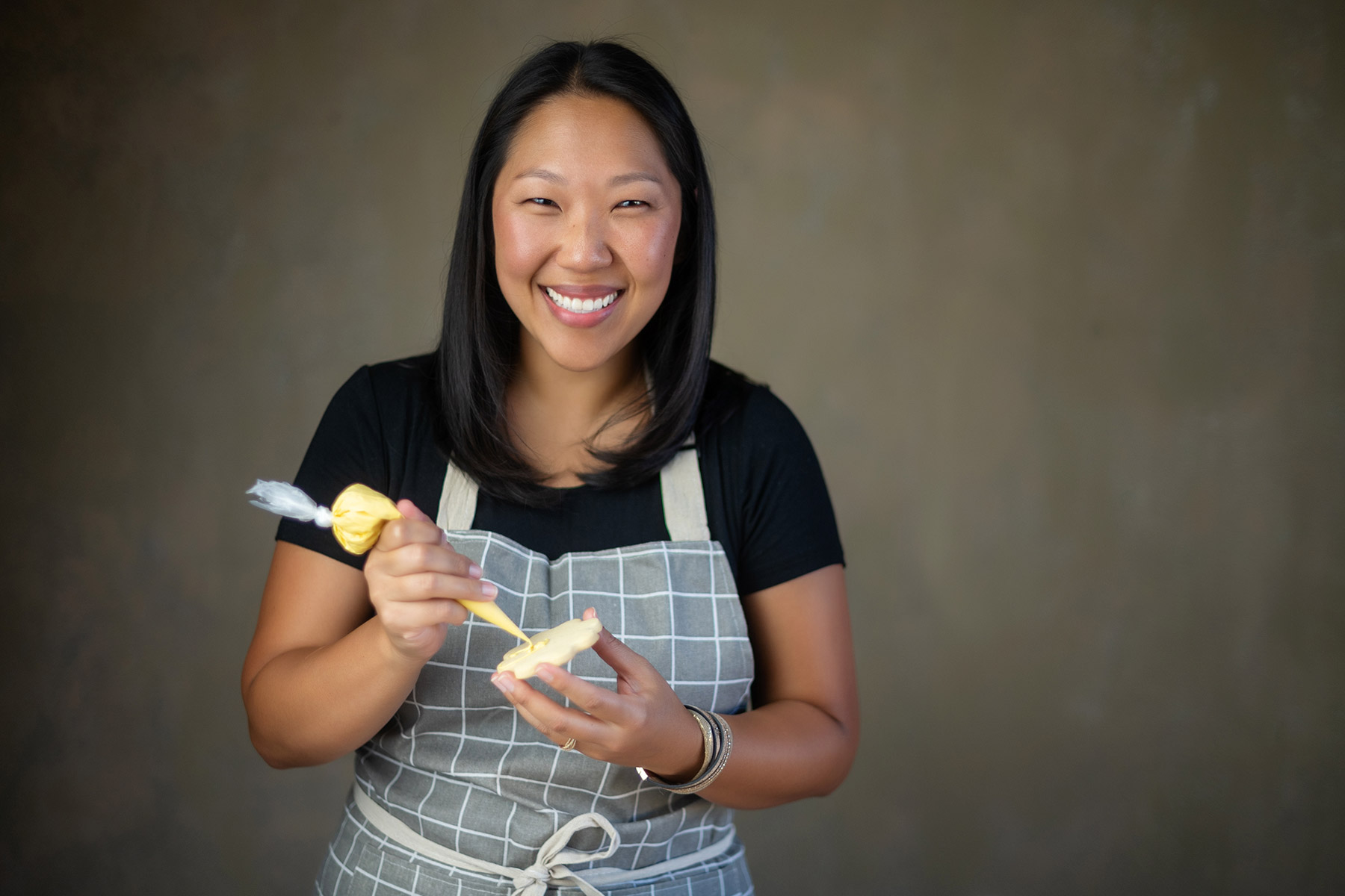 Becca Cairns of Enjoy LLC with a cookie and yellow frosting tube against a brownish background