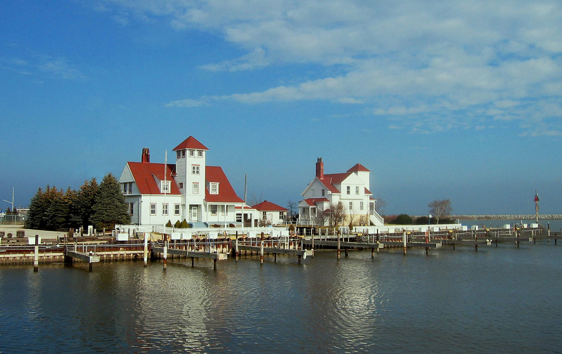 A harbor in Racine, Wisconsin that focuses on two white buildings with red roofs. Lake Michigan is seen in the bottom of the photo, and dark wispy clouds are in the sky in the top center and right.