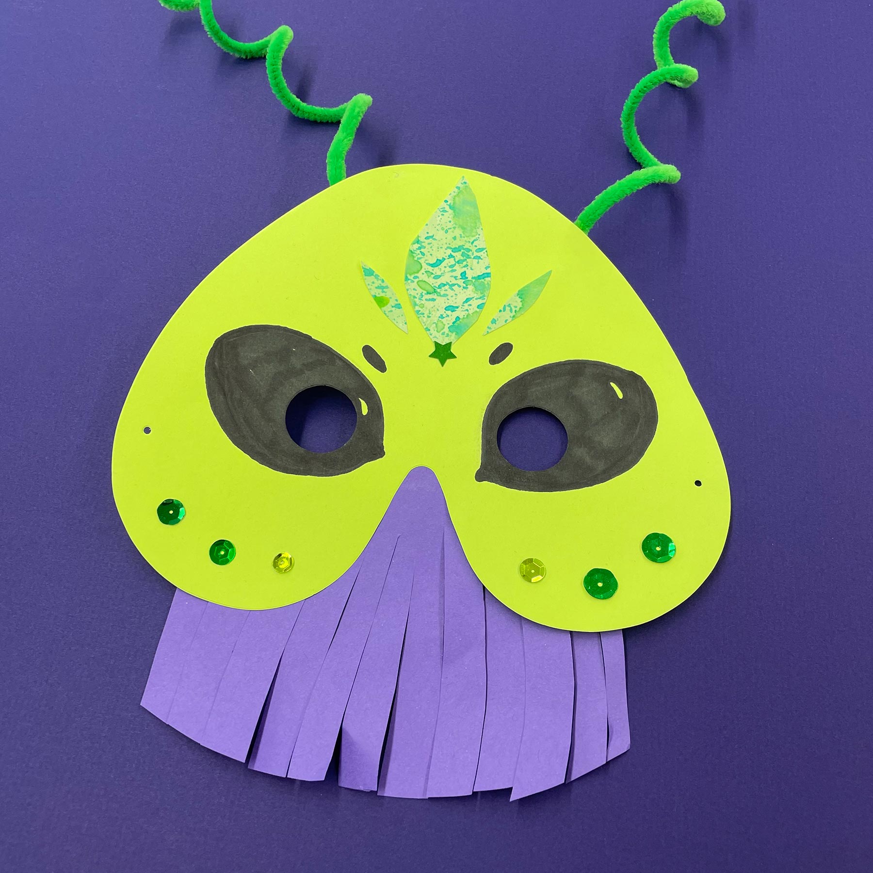 Green and purple paper mask shaped like a fantastical alien creature