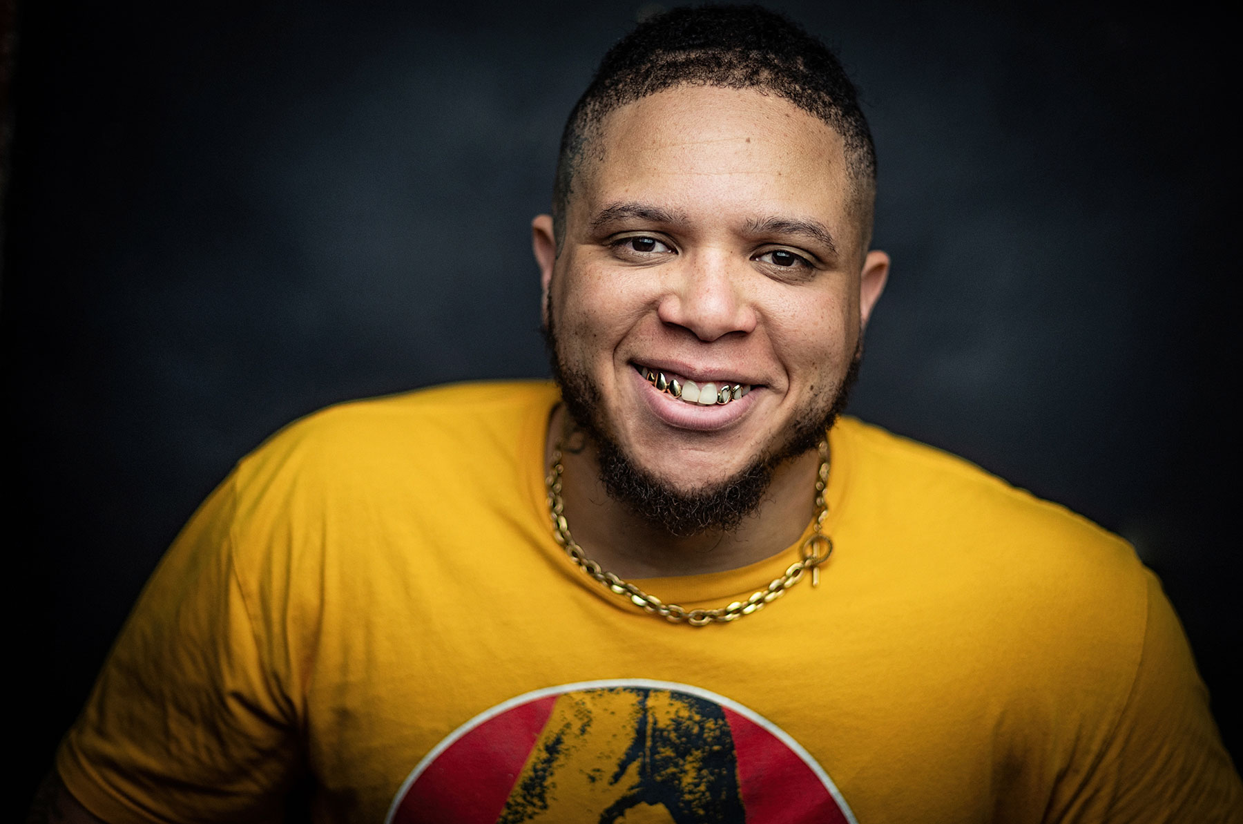 Racine artist Dee Hutch wearing a yellow shirt with a gold chain while smiling at camera