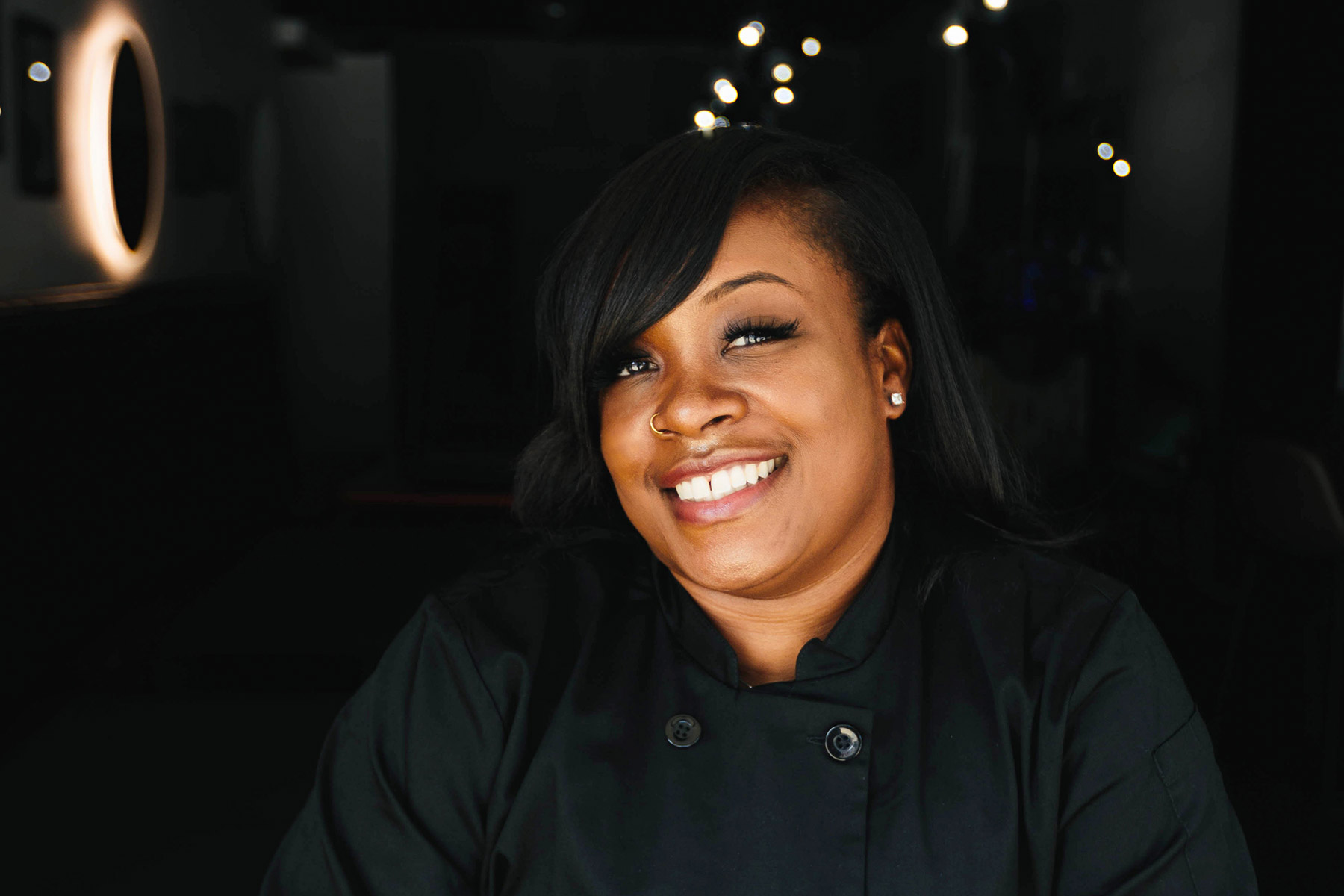 Chef Tasia White of TaejaVu's on Main, wearing a black chef jacket against a dark restaurant backdrop