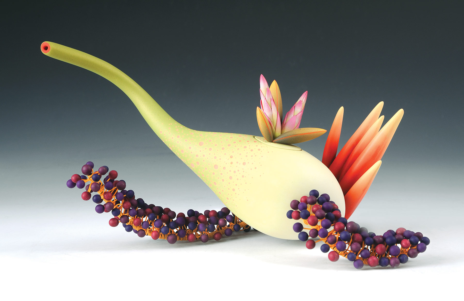 Organic light green teapot with an elongated spout as well as orange and pink leaves on the top and back. Red and purple berry-shaped decorations extend out of the bottom into two spiraling appendages.