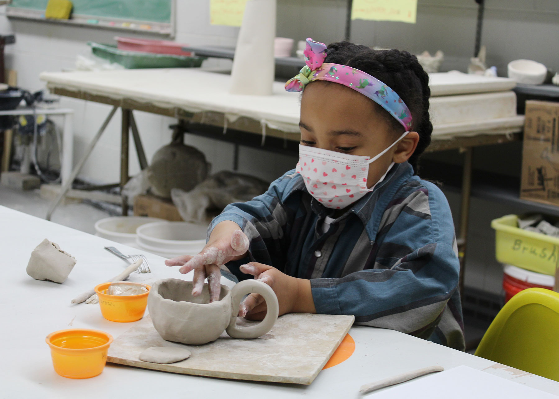 Young girl with a face mask hand building a ceramic mug