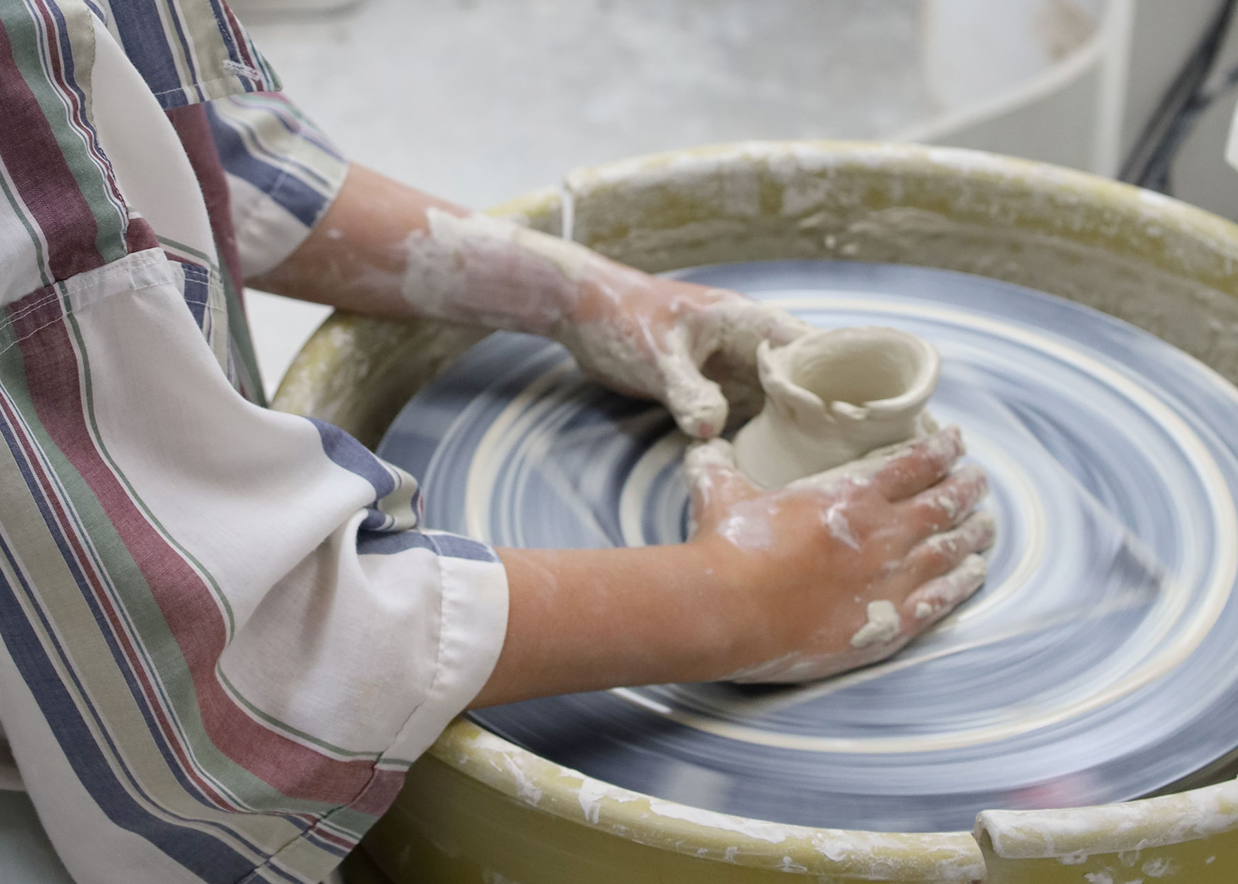 Clay-covered hands forming a vessel on a potters wheel