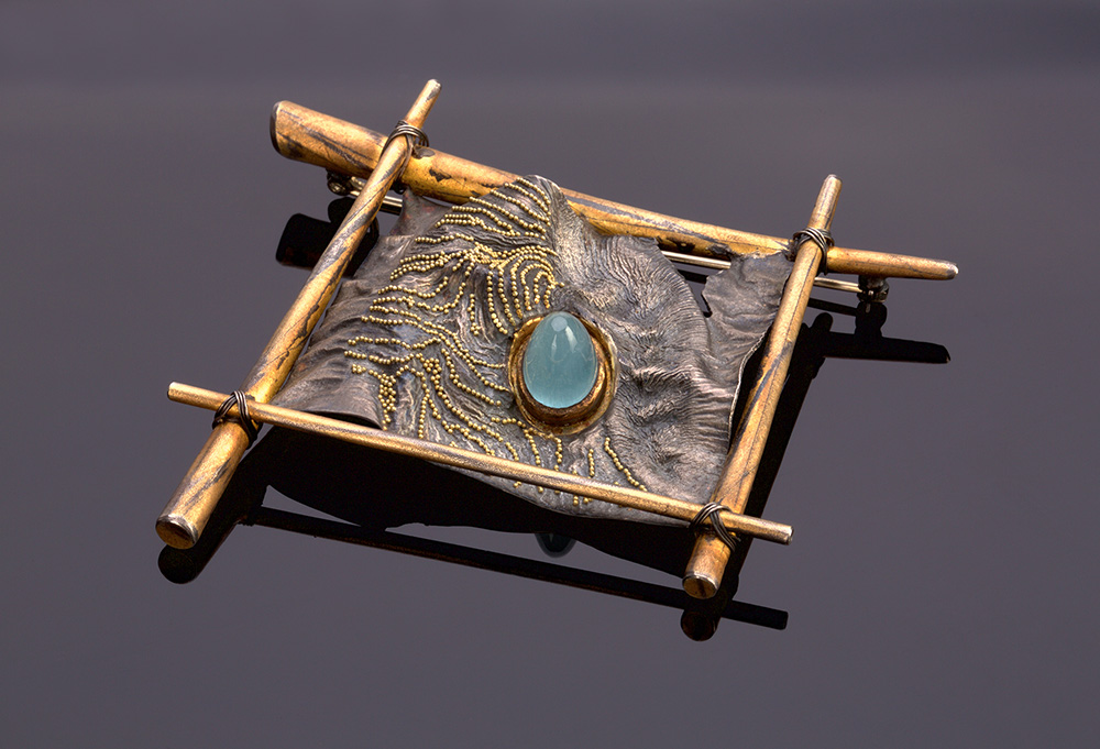 Rectangular brooch with an organic mountain shape in the middle, containing an aquamarine stone