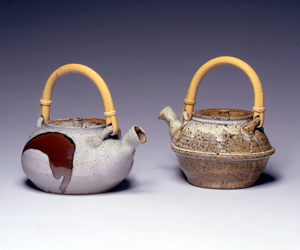 two stoneware teapots with rounded wood handles on the top
