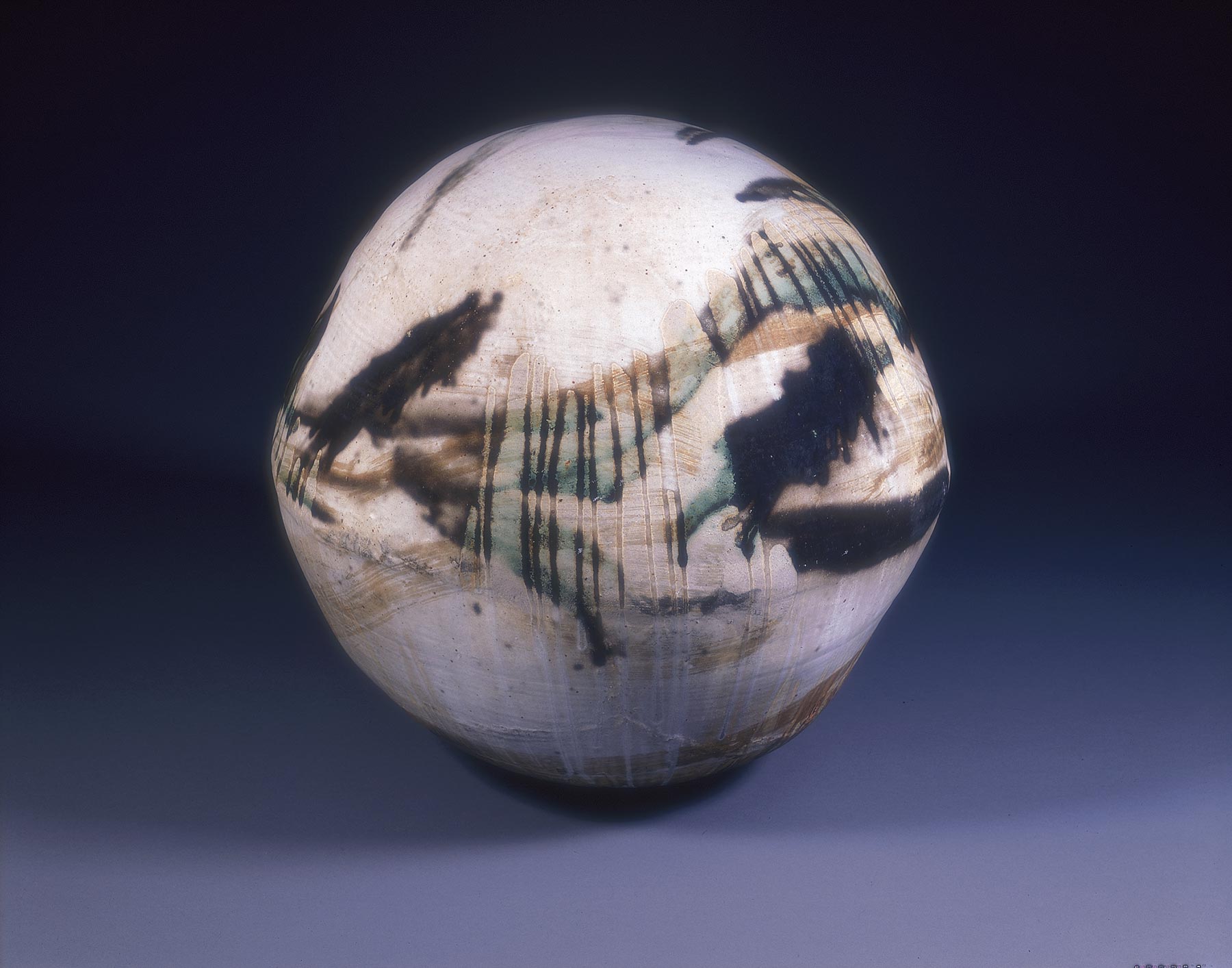 Spherical stoneware object covered in loosely applied, brushstroke-like black, brown, and green glazes.