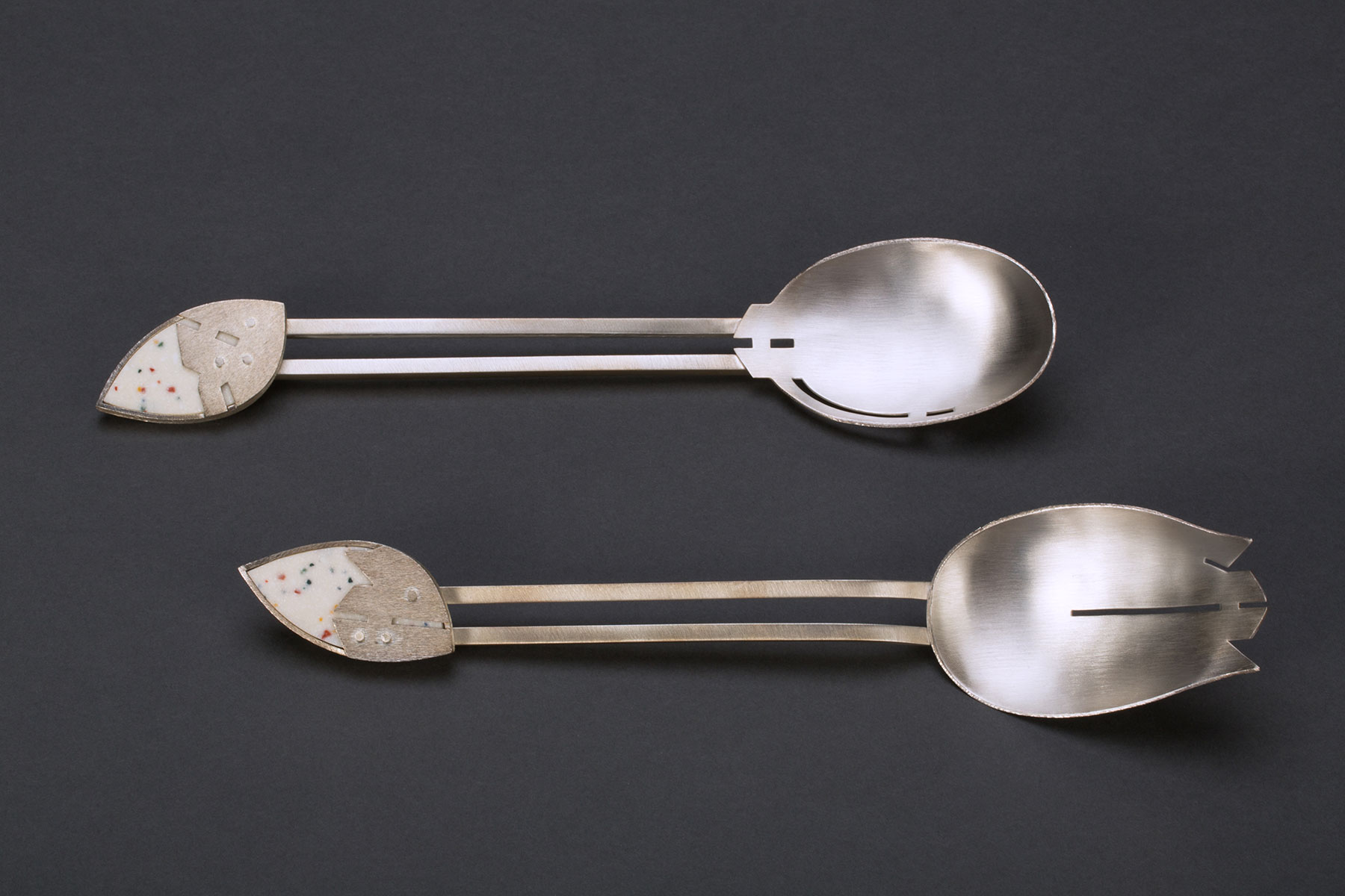 Two silver salad servers—one rounded and one jagged—with an eyeball-shaped adornment at the end