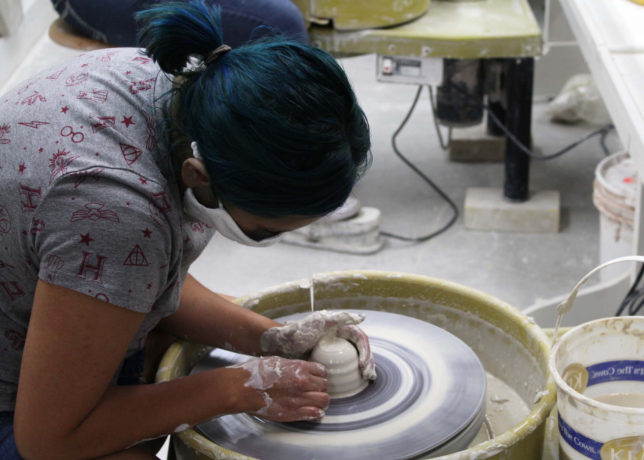 Woman shaping a small form on a potter's wheel